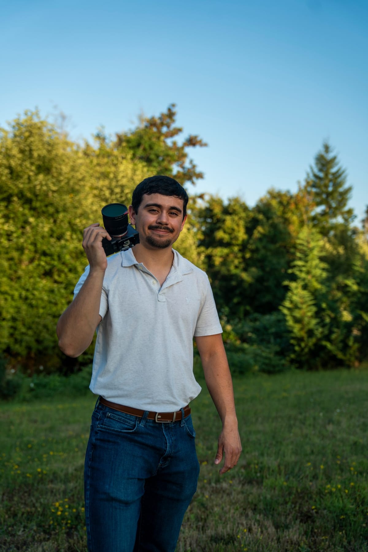DJ Riley smiling in a meadow with his camera resting on his shoulder