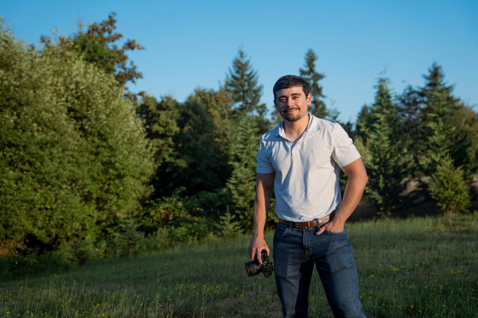 DJ Riley, owner of NW Drone & Media, standing in a meadow with his camera
